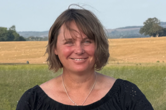 A woman with cropped brown hair smiles in the countryside